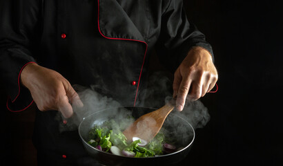 The cook prepares vegetables in a frying pan. The concept of cooking healthy vegetarian food and meals on a black background. Free advertising space