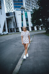 a beautiful girl walks around the city among houses and cars, in a pink dress and white sneakers