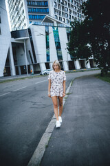 a beautiful girl walks around the city among houses and cars, in a pink dress and white sneakers