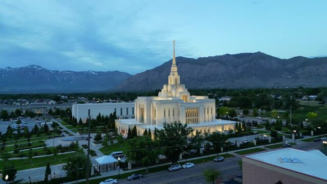 LDS Mormon Temple in Ogden Utah drone flight flying at dusk on beautiful summer night wide shot flying towards beautiful religious temple building with blue skies and mountains in background.