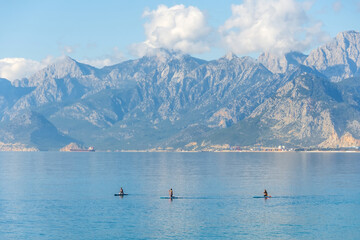 Amazing landscape on rocky mountains with a ship in the sea in the distance and cumulus clouds, sap sup board surfers athletes people swim on boards on the water