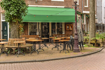 an outdoor cafe with tables and chairs on the sidewalk in front of a brick building that has green awnings