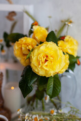beautiful bouquet of yellow garden roses in a glass vase on a light background. There are daisies on the table nearby. Summer still life with flowers. Close up, selective focus