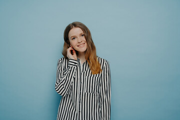 Tender cute European teen girl in striped white shirt, tilting head with hair behind ear,...