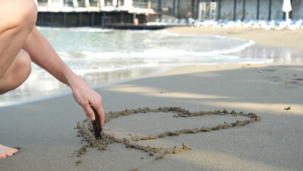 woman drawing heart shape on sea sand