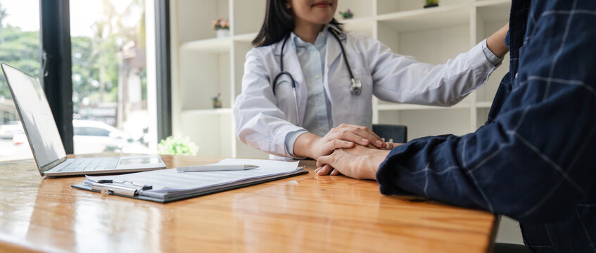 Asian Man Visiting Doctor, Getting Optimistic News After Medical Checkup, Therapy. Young Asian Woman Doctor Holding Hand Of Patient, Giving Hope, Support, Congratulating On Goor Treatment Result