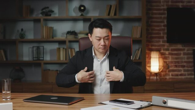 Asian businessman getting ready for important interview and adjusting suit. Successful entrepreneur of middle age working in upscale office with modern remote gadgets on table.