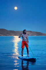 Man at Sup board against full moon at lake