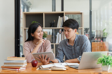 Fototapeta premium Education, teaching, learning, technology and people concept. Two Asian male and female students classmates with helps friend do homeworks learning in classroom, Tutor books with friends