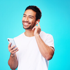 Asian man, earphones and smartphone in studio for music, podcast app and blue background. Happy...