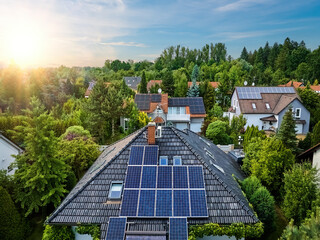 Aerial view of the roofs of houses covered with solar panels. Family houses in gardens, photovoltaic panels on the roof, summer, blue sky with setting sun. Home Electricity Generation, green living.