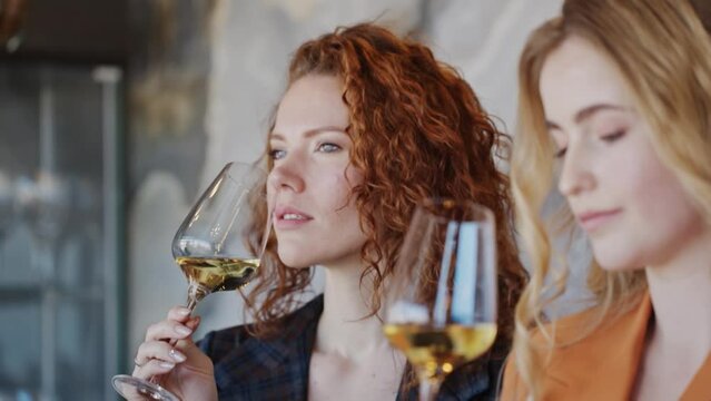 Beautiful women drinking tasting wine in restaurant. Wine expert holding glass of white wine. Slow motion video.