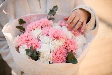 Freshly made bouquet of pink, white carnations decorated with eucalyptus branches and pink feathers in woman's hands