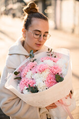 Young woman holding freshly made bouquet of pink, white carnations decorated with eucalyptus branches and pink feathers