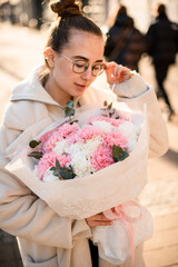 Woman florist holding flower bouquet of pink, white carnations and eucalyptus branches formed in white wrapping paper