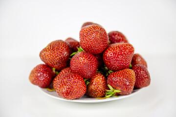 Strawberries of bright red color in a pile on a plate isolated on a white background. Raw organic fruits. Useful products.