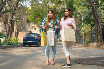 Female friends walking on street after shopping and giving happy expression.