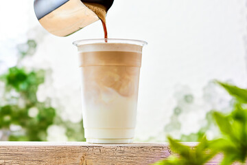 カフェラテ、プラスチックコップに入ったミルクにコーヒーを注ぐ - obrazy, fototapety, plakaty