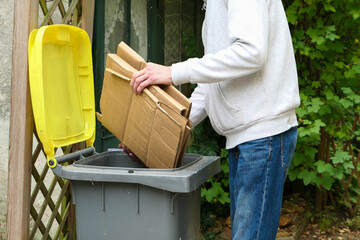 A person who sorts packaging waste. Man putting packing boxes into yellow bin for recycling