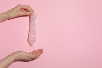Unfolded condom in hand on pink background, place for text