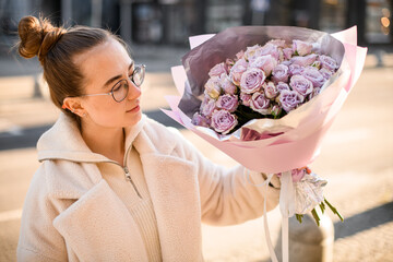 Cute girl posing outdoors with nice delicate bouquet or purple roses in pink wrapping paper