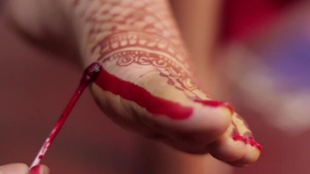 An Indian lady is putting Alta on her foot using a cotton swab - Indian rituals  marriage customs. A Bengali bride is applying a colorful red dye to her Henna / Mehendi decorated foot - an auspicio...