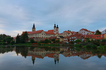 Naklejka na ściany i meble Scenic morning cityscape of medieval town of Telc in the Czech Republic. The castle and colorful buildings reflected in calm water in the lake. Travel and tourism concept. UNESCO World Heritage Site