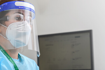 Nurse with protective glasses and N95 mask working on a computer in doctor's office