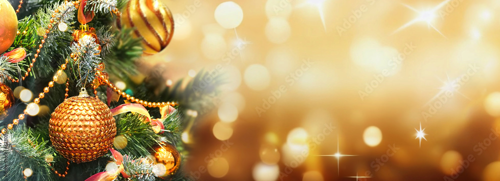 Wall mural Christmas Tree With gold Baubles close-up against backdrop of golden sparkling Christmas lights. Wide format banner. Background with atmosphere of celebration and magic.