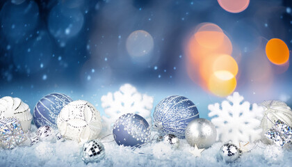 Winter background with Christmas toys in snow, snowflakes, with beautiful light and bokeh on blue sky in evening, copy space. Christmas decoration.