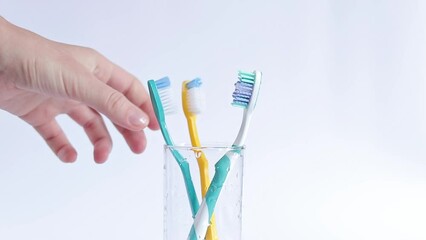A woman's hand takes a toothbrush. Toothbrushes in a glass beaker on a white background. Oral hygiene. Teeth cleaning, caries prevention. The concept of personal hygiene for every day