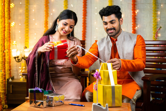 Happy young indian couple packing gift boxes for festival celebration at home - concept of Indian culture, diwali presents and special occasion