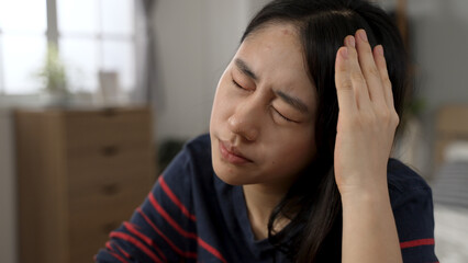 closeup view of a stressed Asian school girl learning from home is rubbing her head while suffering a painful headache.