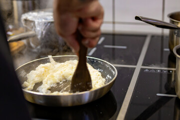 man chef cooking tasty scrambled eggs in frying pan on kitchen