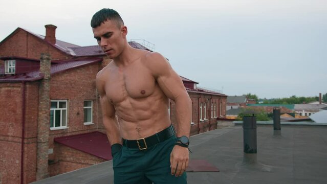 Bodybuilder with naked torso turns on tabata on his phone and rotates kettlebell around his body. Strength training concept