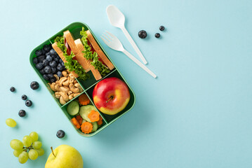 An appealing and health-conscious school lunch scene captured from above. The lunchbox features delectable sandwiches and fresh snacks on a blue background, offering copyspace for text or advertising - obrazy, fototapety, plakaty