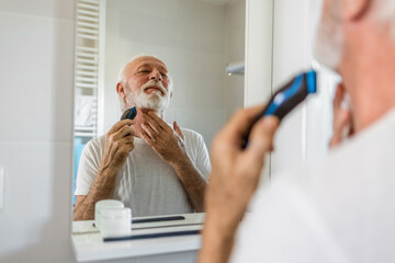 Hand, beard and shaving with an electric razor with a mature man in the bathroom. Face, grooming...