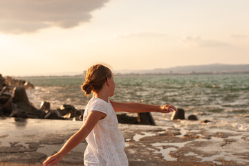 Fototapeta na wymiar Cute girl whirl on the seashore. The sea is not calm the girl is happy and smiling. Dressed in a white dress