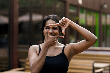 young black person looking in the camera through a frame made of fingers, happy emotions