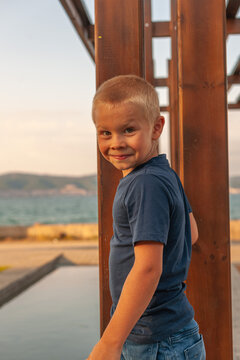 Little boy eks, smiling at the playground. Against the backdrop of the sea at sunset. wearing a blue t-shirt and shorts
