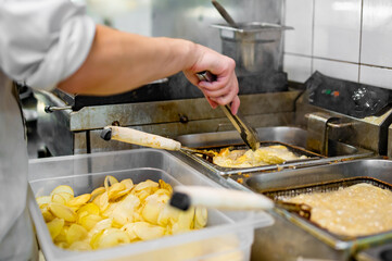 Chef cooking delicious potato chips in hot oil on kitchen