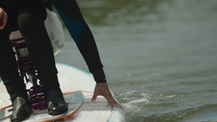 Cropped shot of unrecognizable man with disability sitting on adaptive wakeboard while practicing watersports outdoors in summer