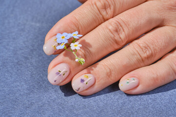 Hands of a woman with a manicure. The nails are covered with gel polish and flowers. Nail design. Concept of spring - summer gel polish coating. Shallow depth of field