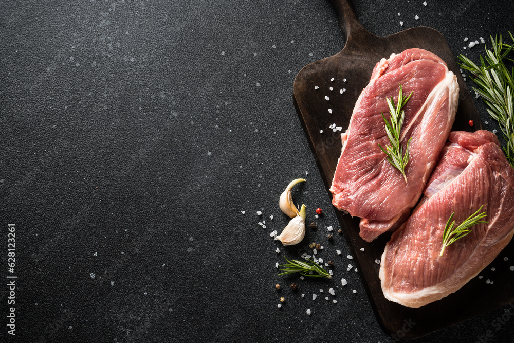 Poster Raw meat steaks with spices at dark background. Top view with space for text.