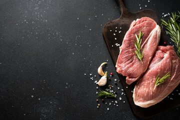Raw meat steaks with spices at dark background. Top view with space for text.