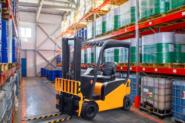 Forklift in stock. Logistics center. Forklift among storage racks. Machine for moving pallets around warehouse. Yellow forklift. Warehouse of chemical products. Industrial tanks on racks