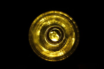 Boquilla de una botella plástica de agua mineral  con retroiluminación amarillo de forma redonda,  formando un original diseño abstracto en círculo brillante con fondo negro