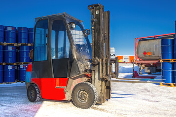 Forklift in industrial area. Territory oil factory. Forklift for unloading barrels. Open-air petrol warehouse. Closed forklift on winter street. Logistics of petroleum products. Industrial machinery