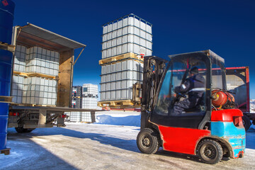 Logistics machines. Forklift is loading truck. Pallets with containers are being prepared for transportation. Territory of logistics center. Forklift with plastic tare in lathing. Shipping, delivery