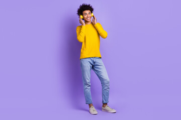 Full length photo of cheerful guy wear stylish sweatshirt arms touching headphones listen playlist isolated on violet color background